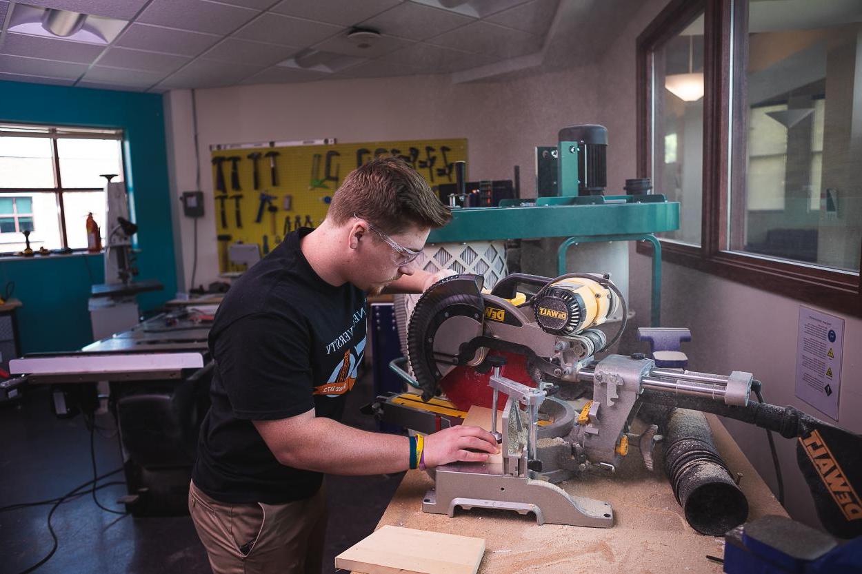 在工程和物理系的实验室里，24岁的杰里米·奥尔盖耶(Jeremey 所有geyer)用圆锯修剪一块木头.